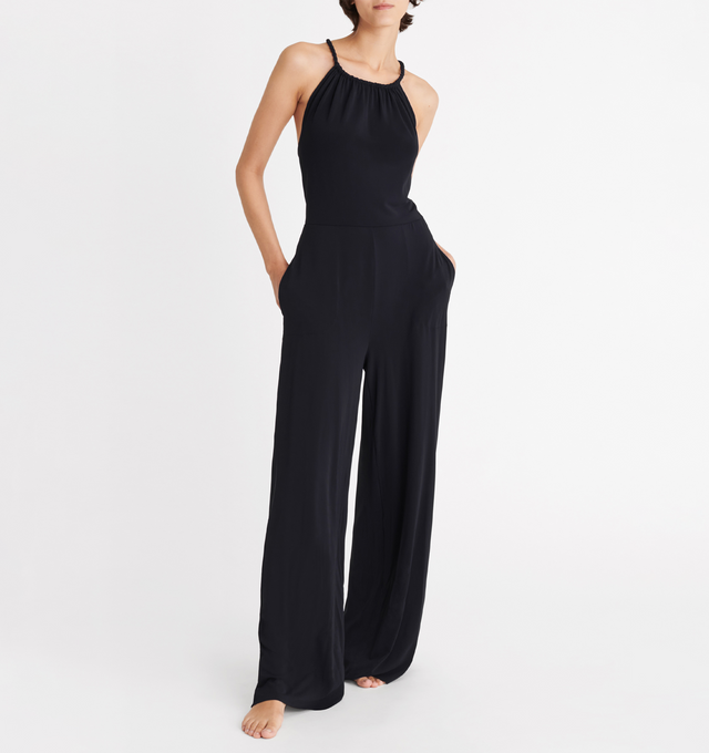 Image 3 of 5 - BLACK - ERES Donna Jumpsuit featuring sliding and twisted link to tie around the neck, adjustable straps crossed in the back, high neckline with shirring, open back and two side pockets. 94% Polyamid, 6% Spandex. Made in France.  