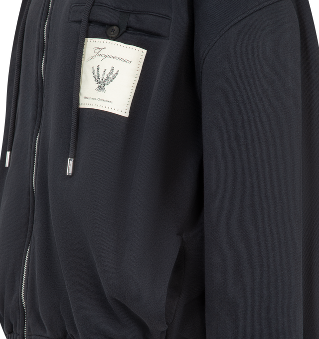 Image 3 of 3 - BLACK - JACQUEMUS Torneo Hoodie featuring rosemary label zipped hoodie, oversized fit, brushed cotton fleece, hood with drawstrings, square metal tips with engraving, drawstring hood with circle and square tips, double-sided zipper, buttoned welt pocket with "J" loop, embroidered Rosemary logo patch, side-seam pockets, elasticated cuffs and hem, embroidered logo patch on the back and fully lined. 100% cotton. Made in Portugal. 