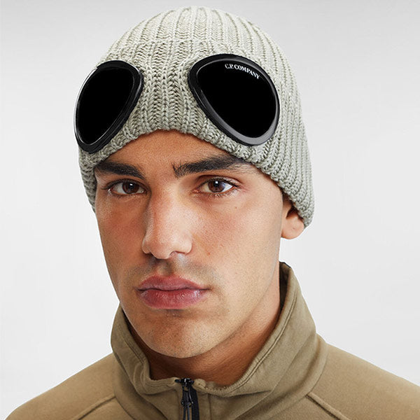 Man wearing C.P. Company grey beanie with goggle detail, available online.