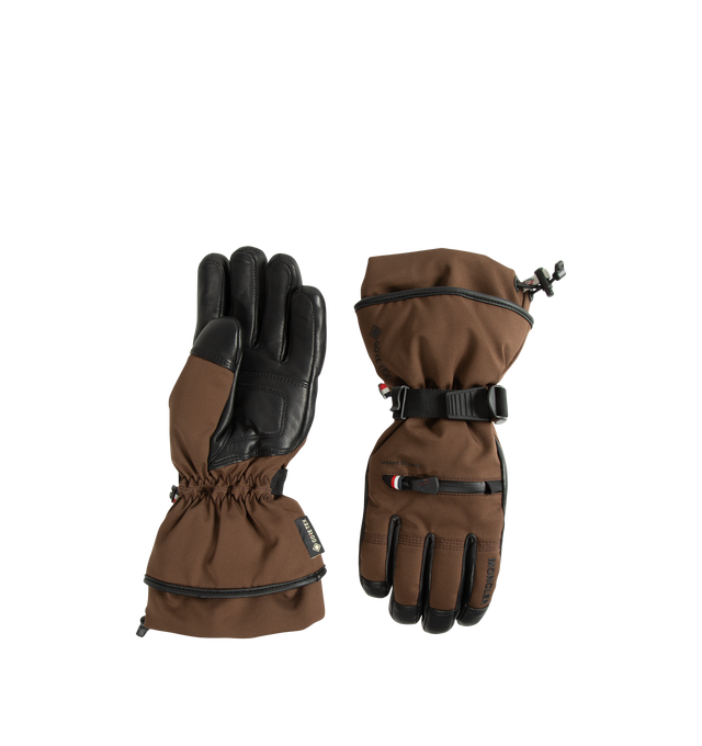 Image 1 of 3 - BROWN - Moncler Grenoble Women's Padded Gloves are crafted from a 4-way stretch technical nylon blend and feature a performance-driven design created in collaboration with Reusch. Engineered for mountain sports and ski conditions, these insulated gloves provide warmth and protection while leather reinforcements at the palms and fingertips enhance grip. Finished with a zipped pocket designed to hold a heating pad, adjustable cuffs, and a signature silicone logo patch. Main Material: 87% Polyam 