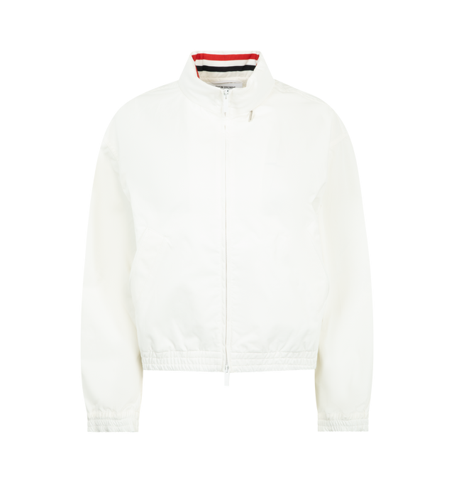 Image 1 of 4 - WHITE - THOM BROWNE Nylon Tech Track Jacket featuring front hidden two-way zip closure, stand collar lined with RWB grosgrain, ripstop drawstring hood that folds into collar with hidden zip, welt hand pockets with hidden snap, back storm flap over mesh panel, RWB grosgrain trim along storm flap and back sleeves, elasticated cuffs and hem with channel stitching and signature striped grosgrain loop tab. 51% polyamide, 49% cotton. Made in Italy. 