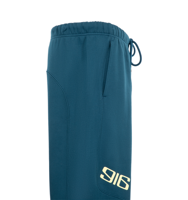 Image 3 of 3 - BLUE - Fear of God ESSENTIALS Classic Moto Sweatpant is crafted from heavyweight 380 GSM cotton-blend fleece and features a relaxed classic-fit silhouette with motocross-inspired seam detailing. Designed with signature 916 puff-print graphics at the front and FGX puff-print graphics extending down the back of the legs, this elevated sweatpant is finished with an encased elastic waistband, internal drawstring, elasticized cuffs, and side-seam pockets for everyday comfort and functionality. Mai 