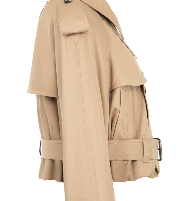 Image 3 of 3 - NEUTRAL - JW Anderson Women's Cropped Trench Coat is crafted from water-resistant cotton and features a cropped, boxy-fit silhouette that reinterprets the classic trench coat with a contemporary proportion. Designed with traditional trench details including a gun flap, throat latch, storm shield, self-fabric belt at the waist and cuffs, welt pockets, horn buttons, and a full cotton lining. Main Material: 100% Cotton. Lining: 100% Cotton. Made in Italy. 
