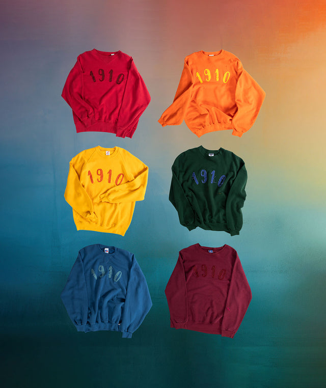 6 Transnomadica crewneck sweatshirts - Red, Orange, Yellow, Green, Blue, Burgundy, each with a 1910 applique on the chest