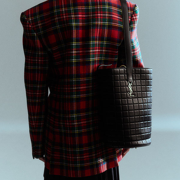 Woman's back in red plaid blazer carrying black quilted leather bag by Saint Laurent, available online.